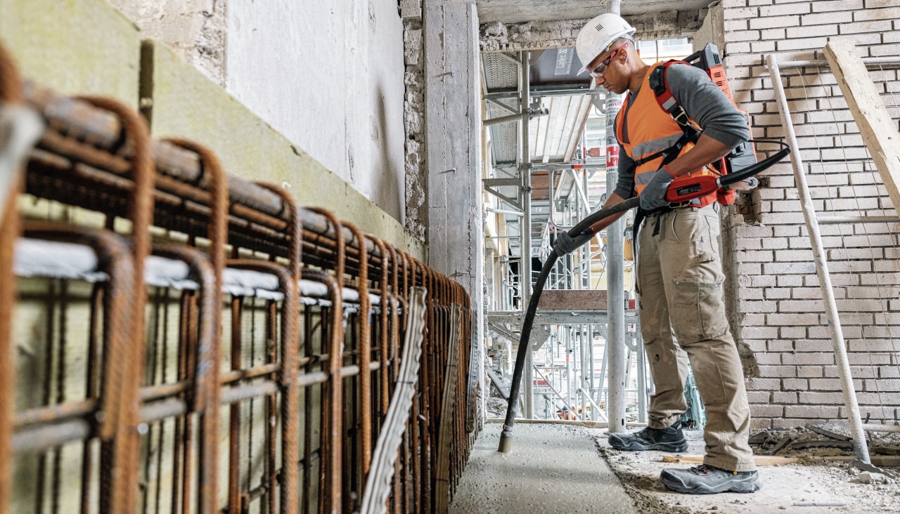 Worker using the NCV Cordless concrete vibrator indoors, vibrating a strip of concrete, free of gas fumes.